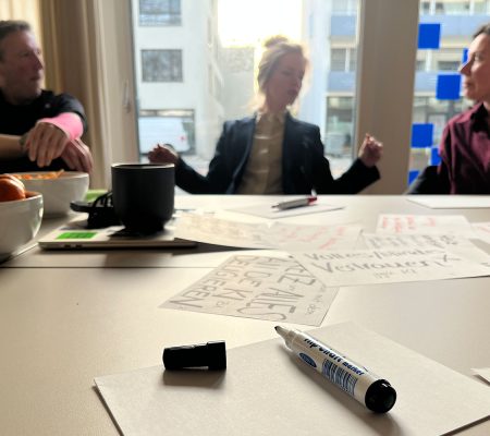 Tischfläche mit Stift und Papier, Personen im Hintergrund sitzend